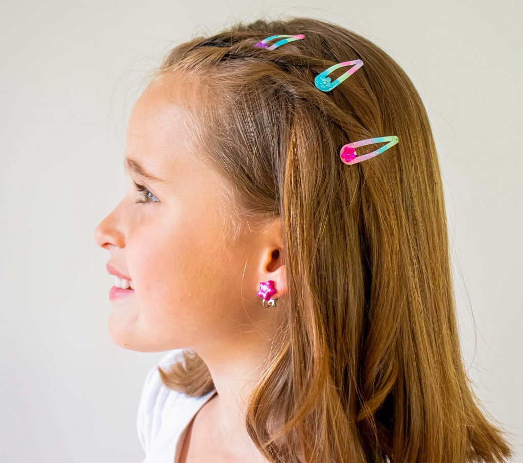 Mädchen mit drei bunten Haarspangen und pinkfarbenem Ohrschmuck